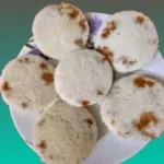 A plate of freshly made Bhapa Pitha, which are fluffy white steamed rice cakes with spots of sweet date jaggery.